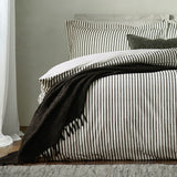Hebden Cotton Melange Duvet Cover Set in black and cream stripe on a bed, styled with matching pillowcases and a chunky black textured throw.