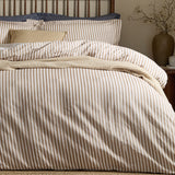 Hebden Cotton Melange Duvet Cover Set in Caramel, shown on a bed with striped cotton bedding, cream cushions and a woven throw in a bedroom setting.