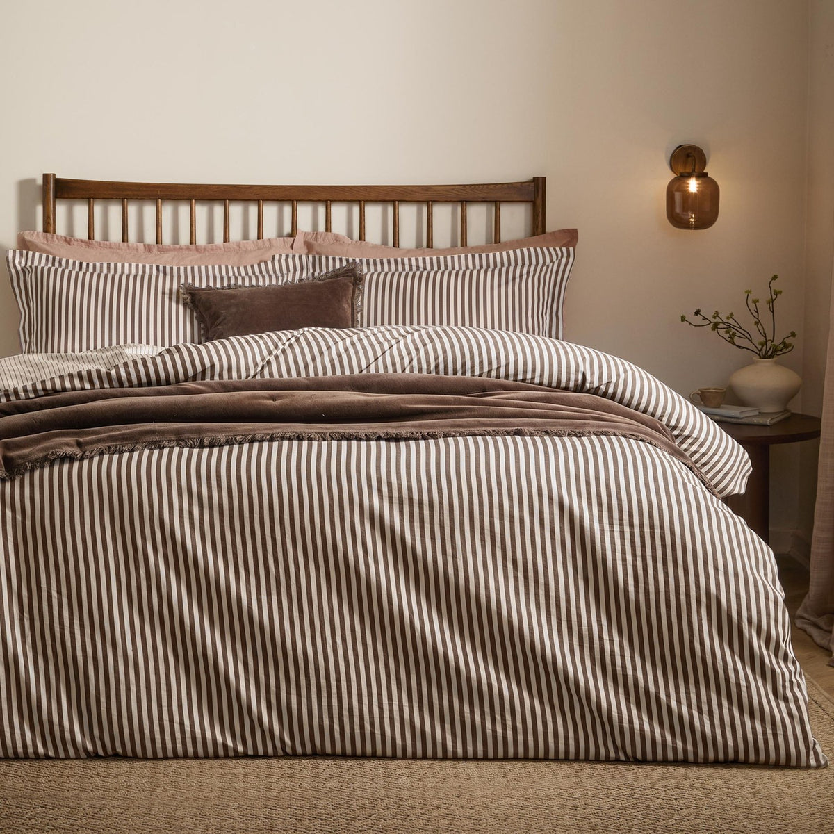 Hebden Cotton Melange Duvet Cover Set in espresso brown stripe on cream, styled on a bed with matching pillowcases and a velvet cushion in a bedroom setting.