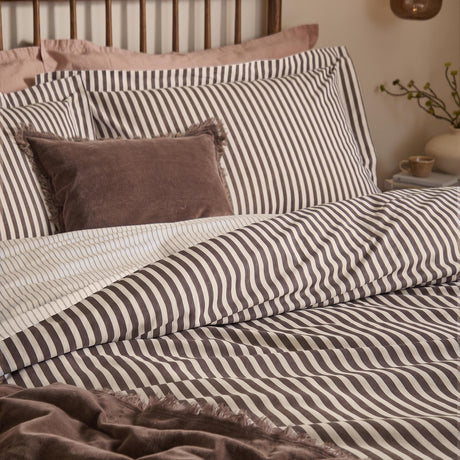 Hebden Cotton Melange Duvet Cover Set in espresso brown stripe on cream, shown on a bed with matching pillowcases and a mauve velvet cushion.