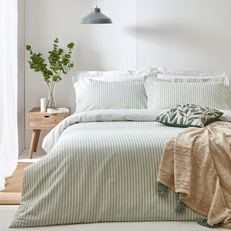 Hebden Cotton Striped Duvet Cover Set in Eucalyptus, styled on a bed with matching pillowcases, a green leaf-print cushion and beige tasselled throw in a light bedroom setting.