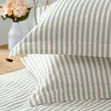 Hebden Cotton Striped Duvet Cover Set in Eucalyptus, shown close-up on pillows and bedding with a woven green and off-white stripe pattern, styled in a bedroom with a vase of flowers.