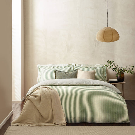 Hebden Cotton Striped Duvet Cover Set in Forest green and cream, shown on a bed with matching pillowcases, cushions and a beige throw in a bedroom setting.