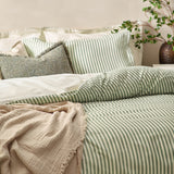Hebden Cotton Striped Duvet Cover Set in Forest on a bed, showing reversible green and cream stripes with matching pillowcases, textured cushions and a beige throw.