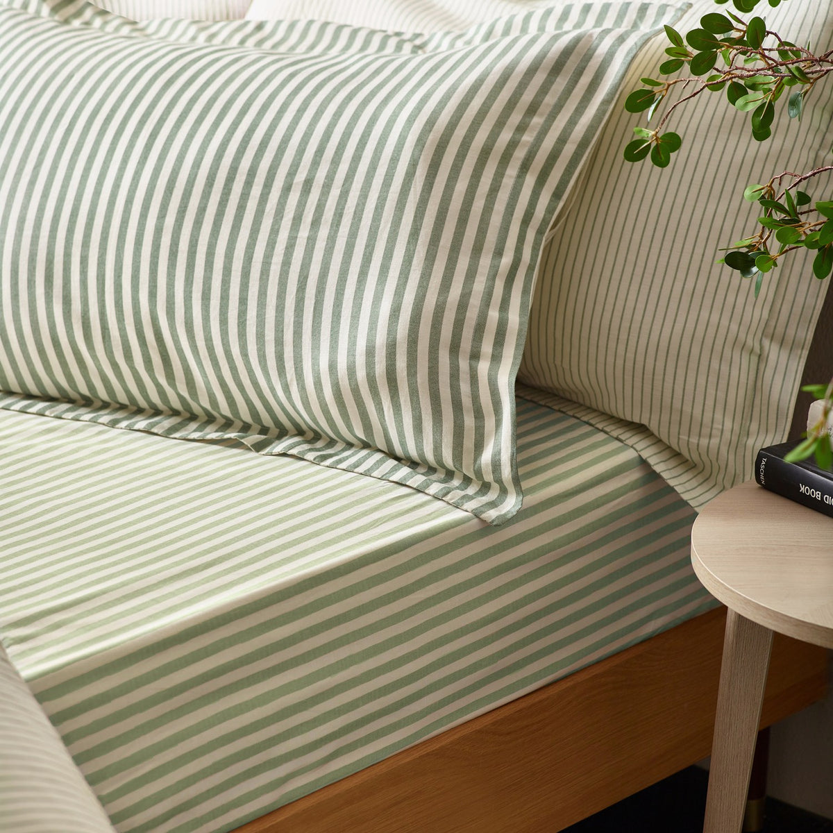Hebden Cotton Striped Duvet Cover Set in Forest green and cream, shown on a bed with matching pillowcases beside a wooden bedside table.