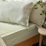 Hebden Cotton Striped Duvet Cover Set in Forest green and cream, shown on a bed with matching pillowcases beside a wooden bedside table.