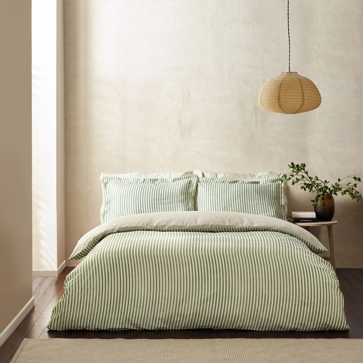 Hebden Cotton Striped Duvet Cover Set in Forest green and cream, styled on a bed with matching pillowcases in a neutral bedroom with a woven pendant light.