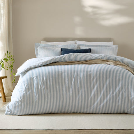 Hebden Cotton Melange Duvet Cover Set in mineral blue stripe on white, shown on a bed with matching pillowcases and a navy accent cushion in a neutral bedroom.