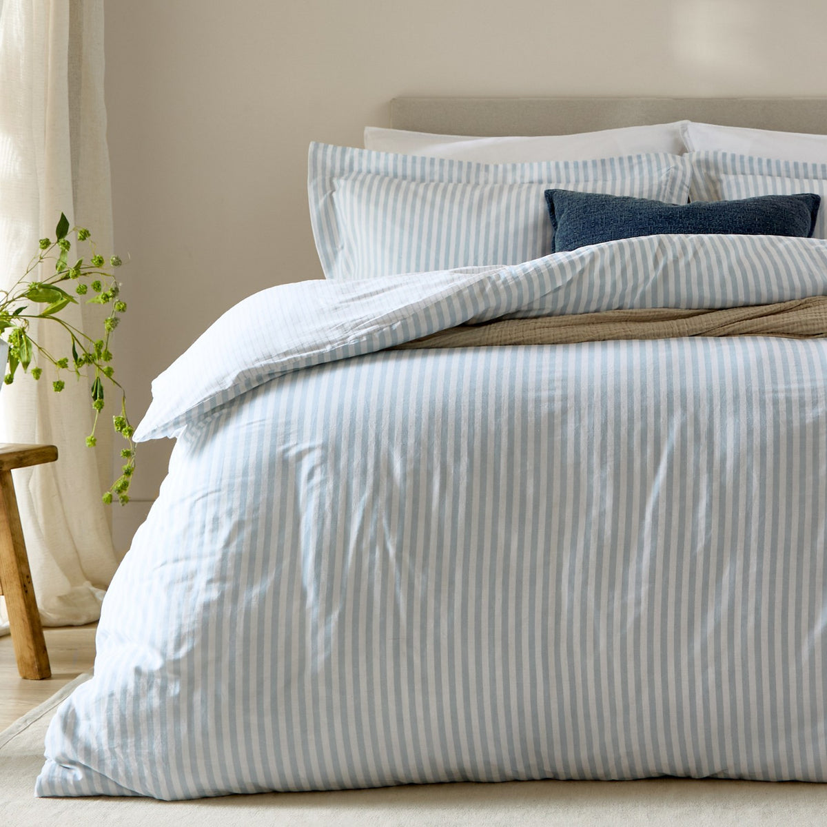 Hebden Cotton Melange Duvet Cover Set in mineral blue, styled on a bed with striped pillowcases, navy cushions, and neutral throws in a bedroom setting.