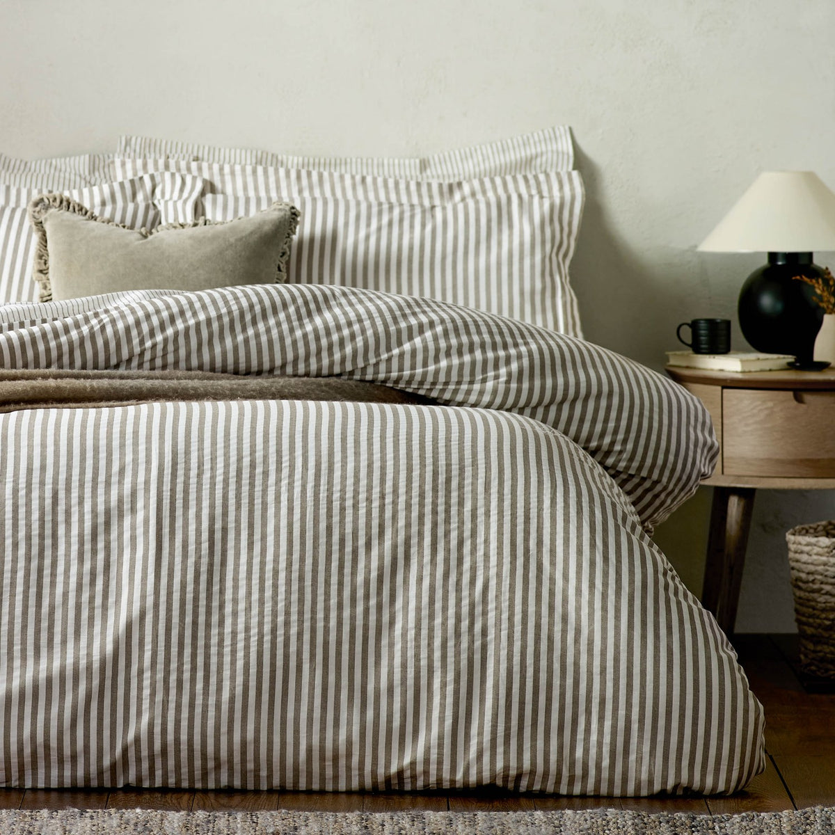 Hebden Cotton Melange Duvet Cover Set in mole brown and white stripe, shown on a bed with matching pillowcases in a bedroom setting beside a wooden nightstand.