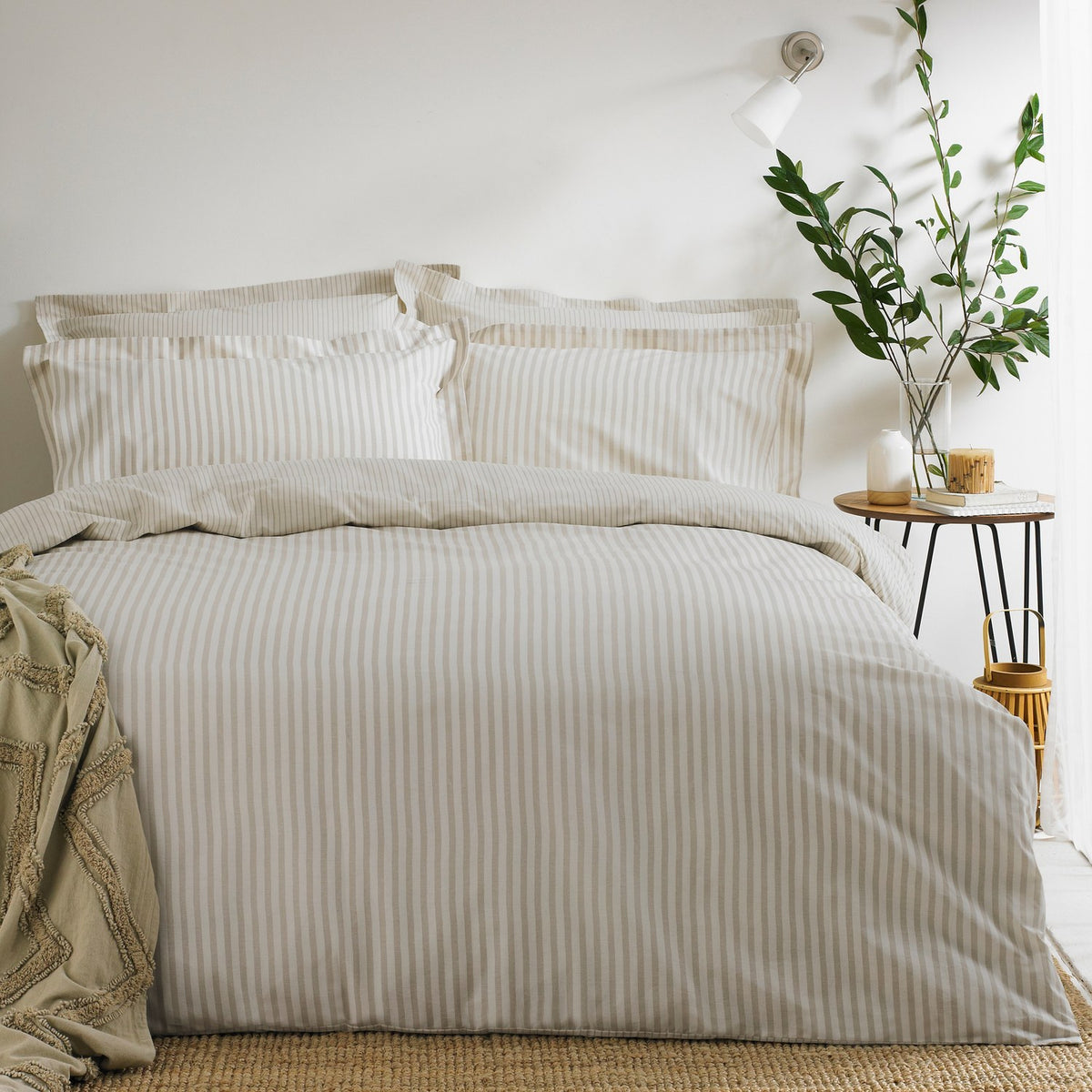 Hebden Cotton Striped Duvet Cover Set in natural beige and cream on a made bed with matching pillowcases, styled in a bedroom with a side table and potted plant.
