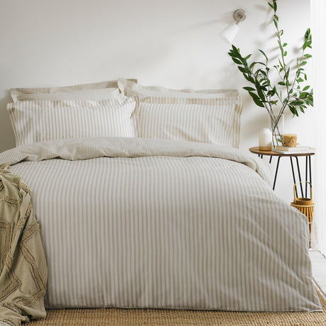 Hebden Cotton Striped Duvet Cover Set in natural beige and cream on a made bed with matching pillowcases, styled in a bedroom with a side table and potted plant.