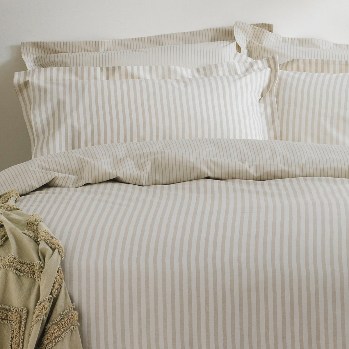 Hebden Cotton Striped Duvet Cover Set in natural beige and cream, dressed on a bed with matching pillowcases and a textured throw folded at the corner.