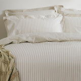 Hebden Cotton Striped Duvet Cover Set in natural beige and cream, dressed on a bed with matching pillowcases and a textured throw folded at the corner.