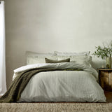 Hebden Cotton Melange Duvet Cover Set in olive green stripe on white, styled on a bed with matching pillowcases and a green textured throw against a neutral bedroom wall.