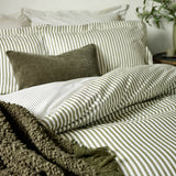 Hebden Cotton Melange Duvet Cover Set in olive green stripe on white, shown on a bed with matching pillowcases, a textured olive cushion, and a bouclé throw.