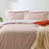 Hebden Cotton Striped Duvet Cover Set in pecan, showing a woven mélange stripe in reddish-brown and white on a bed with matching pillowcases and a beige textured throw.
