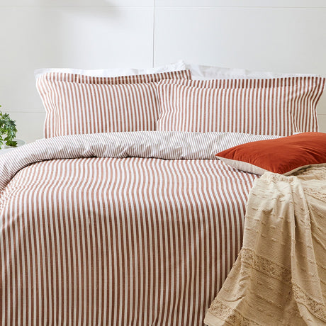Hebden Cotton Striped Duvet Cover Set in pecan, showing a woven mélange stripe in reddish-brown and white on a bed with matching pillowcases and a beige textured throw.