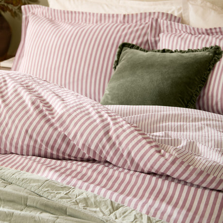 Hebden Cotton Melange Duvet Cover Set in Rosewood on a bed with matching pink and white striped pillowcases, sage green quilted throw, and a green velvet cushion.