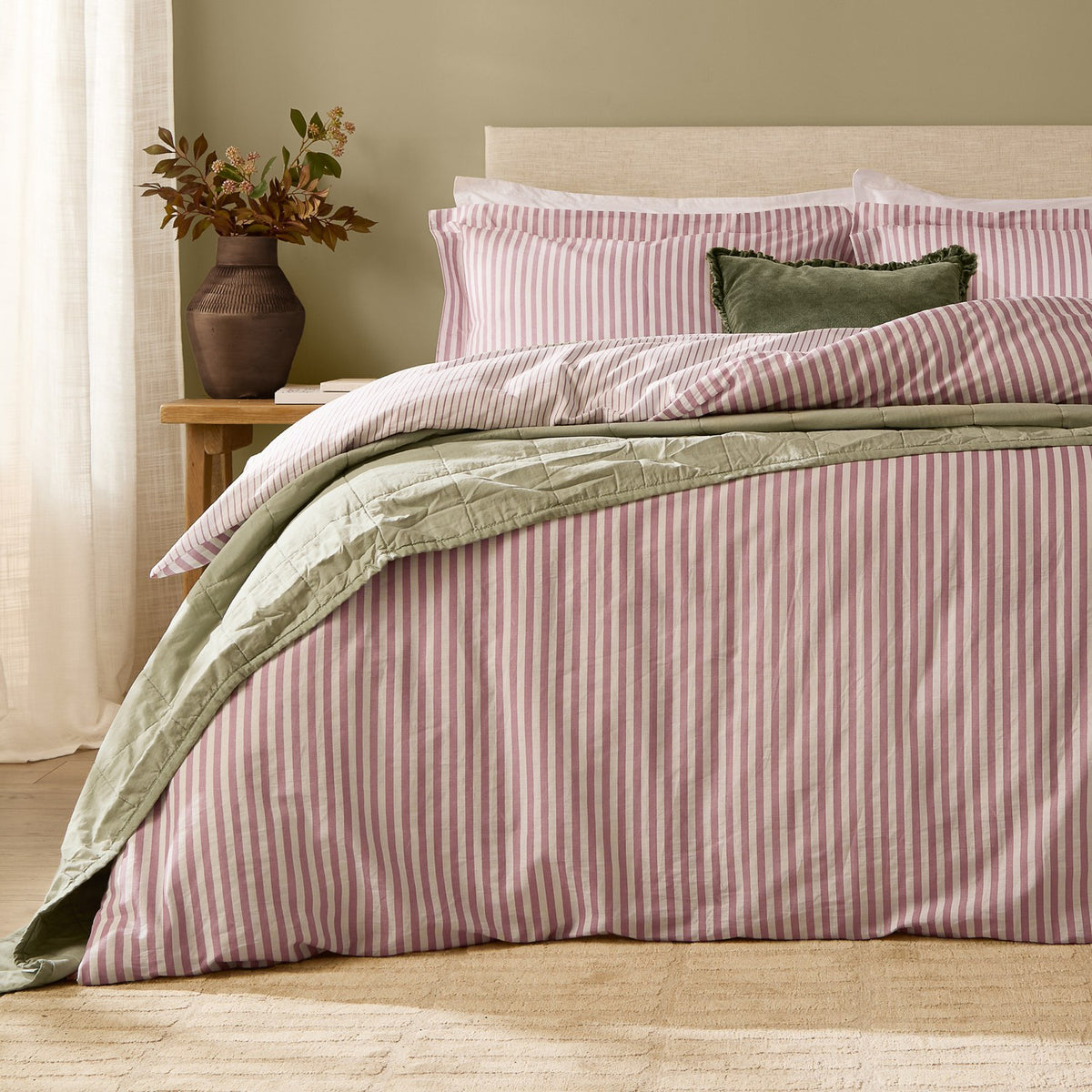 Hebden Cotton Melange Duvet Cover Set in Rosewood pink and cream stripe on a bed with matching pillowcases, styled with a sage green quilt and cushion in a bedroom setting.