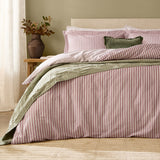 Hebden Cotton Melange Duvet Cover Set in Rosewood pink and cream stripe on a bed with matching pillowcases, styled with a sage green quilt and cushion in a bedroom setting.