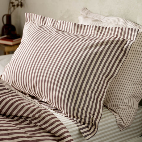 Hebden Striped Cotton Pillowcase Pair in Beetroot, shown on bedroom pillows with matching striped sheets, featuring a chalky red stripe on off-white cotton.