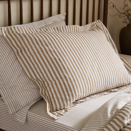 Hebden Reversible Cotton Pillowcase Pair in caramel brown, styled on a bed with matching striped duvet cover, showing the printed melange stripe against white and reversible plain side.