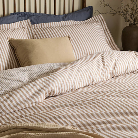 Hebden Reversible Cotton Pillowcase Pair in Caramel, styled on a bed with striped duvet cover, showing the printed caramel and white melange stripe finish.