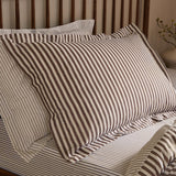 Hebden Reversible Cotton Pillowcase Pair in Espresso Brown, striped brown and cream cotton pillow shown on a bed with a wooden slatted headboard in a bedroom setting.