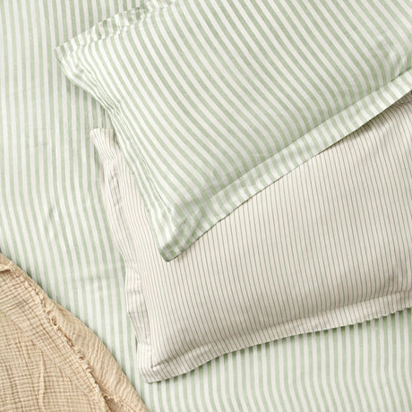 Hebden Melange Cotton Pillowcase Pair in Eucalyptus, showing green and off-white striped pillowcases layered on matching striped bedding with a beige quilted throw nearby.