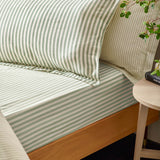 Hebden Melange Cotton Pillowcase Pair in Forest, green and cream striped cotton pillowcases styled on a bed beside matching striped bedding in a bedroom setting.