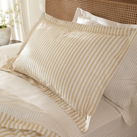 Hebden Melange Cotton Pillowcase Pair in Honey Yellow, striped cotton pillowcases on a bed with a matching striped duvet and cane headboard.