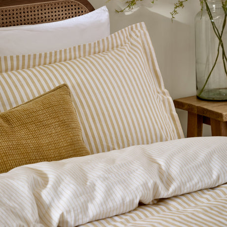 Hebden Melange Cotton Pillowcase Pair in Honey Yellow, striped cotton pillowcases on a bed with a matching striped duvet and mustard textured cushion, near a wooden headboard.