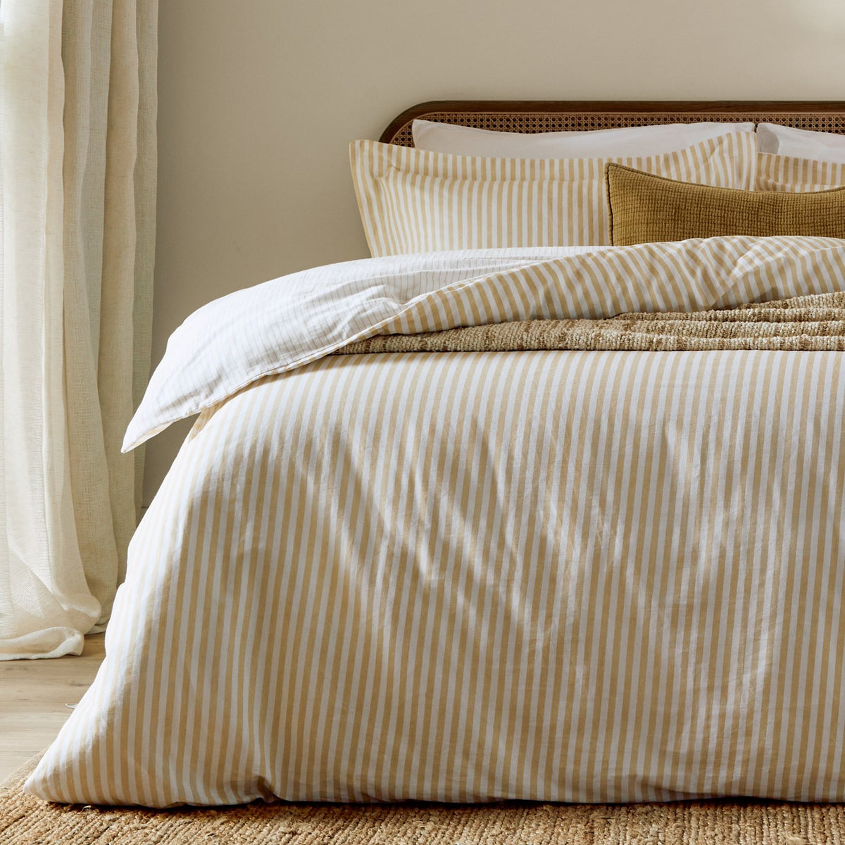 Bed dressed with Hebden Melange Cotton Pillowcases in Honey Yellow, featuring a soft honey-gold striped pattern on cream, paired with a striped duvet cover and mustard textured cushion.