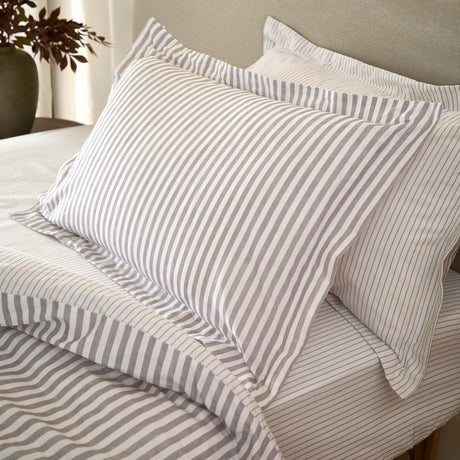 Hebden Melange Cotton Pillowcase Pair in mauve-grey stripe on cream, shown styled on a bed with matching striped duvet and sheets.