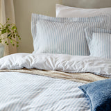 Hebden Melange Cotton Pillowcase Pair in mineral blue stripe on white, styled with white and blue-striped bedding in a bedroom setting.