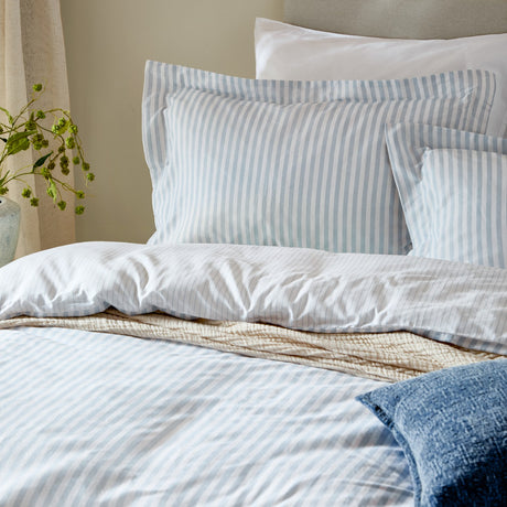 Hebden Melange Cotton Pillowcase Pair in mineral blue stripe on white, styled with white and blue-striped bedding in a bedroom setting.