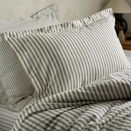 Hebden Striped Cotton Pillowcase Pair in Mole, shown styled on a bed with matching striped bedlinen, featuring mole-brown and white stripes in cotton with a tumbled finish.