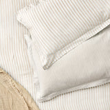 Hebden Melange Cotton Pillowcase Pair in Natural, fine beige stripe on cream cotton, shown layered with a matching striped duvet on a bed.