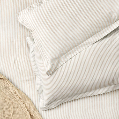 Hebden Melange Cotton Pillowcase Pair in Natural, fine beige stripe on cream cotton, shown layered with a matching striped duvet on a bed.