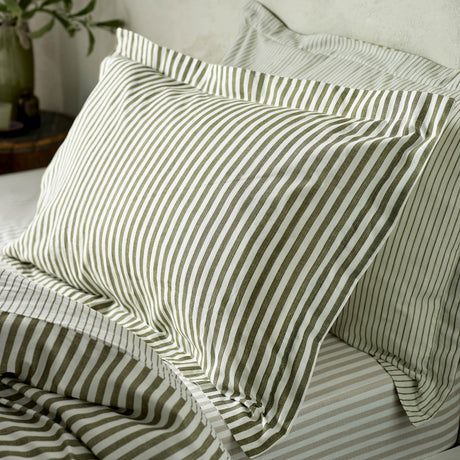 Hebden Striped Cotton Pillowcase Pair in olive and white, shown styled on a bed with matching striped bedding in a bedroom setting.