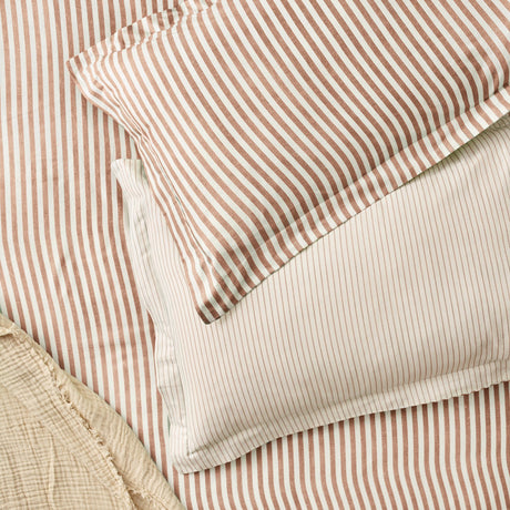 Hebden Melange Cotton Pillowcase Pair in pecan brown, showing closely spaced striped cotton pillowcases layered over matching striped bedding with a cream reverse.