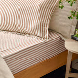 Hebden Melange Cotton Pillowcase Pair in pecan brown stripe on cream, styled on a bed with matching fitted sheet and wooden bed frame.