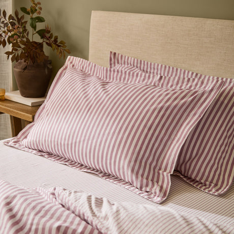 Hebden Striped Cotton Pillowcase Pair in Rosewood, showing two Oxford-bordered pillowcases with rosewood-pink and cream stripes on a bed with matching striped sheets.