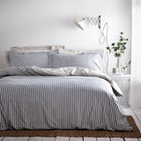 Hebden Cotton Striped Duvet Cover Set in navy on a bedroom bed, with matching pillowcases, a white side table, wall lamp, and vase of flowers.