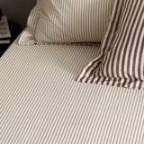 Hebden Striped Cotton Fitted Sheet in Beetroot, cream cotton with narrow muted red stripes, shown fitted to a bed with matching pillowcases.