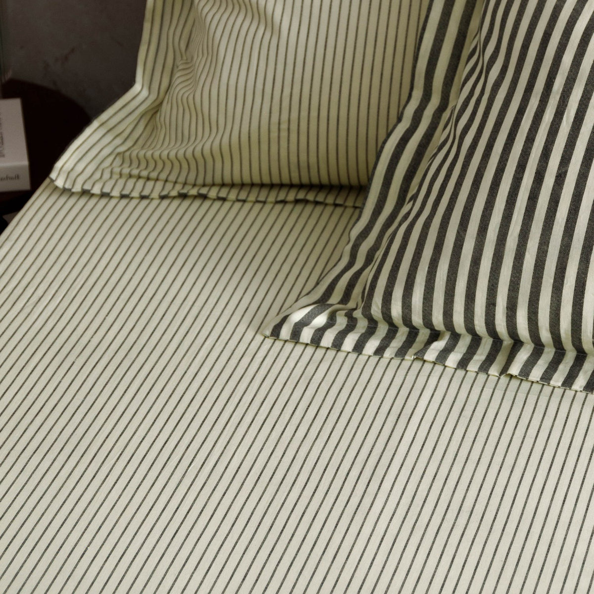 Hebden Striped Cotton Fitted Sheet in Black on bed, showing cream ground with fine charcoal pinstripes across sheet and matching pillowcases.