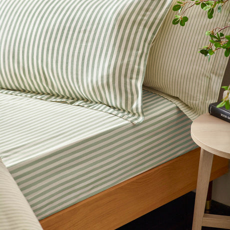 Hebden Melange Cotton Fitted Sheet in Forest green and cream stripe on a wooden bed, with matching pillowcases and a bedside table beside it.