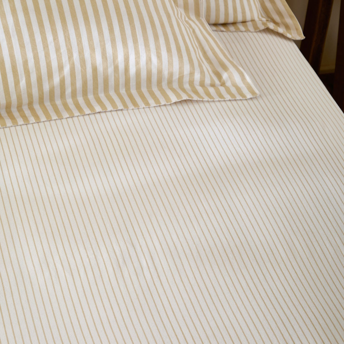 Hebden Striped Cotton Fitted Sheet in honey yellow, showing cream cotton fabric with narrow sandy gold stripes on a fitted bed with matching pillowcases.