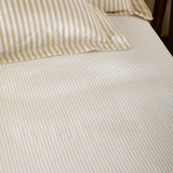 Hebden Striped Cotton Fitted Sheet in honey yellow, showing cream cotton fabric with narrow sandy gold stripes on a fitted bed with matching pillowcases.